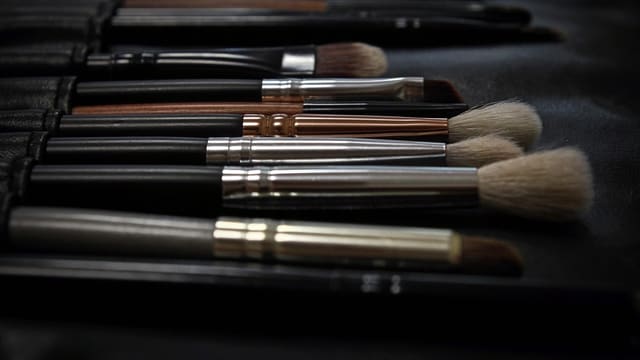 A row of makeup brushes lying on a dark surface.