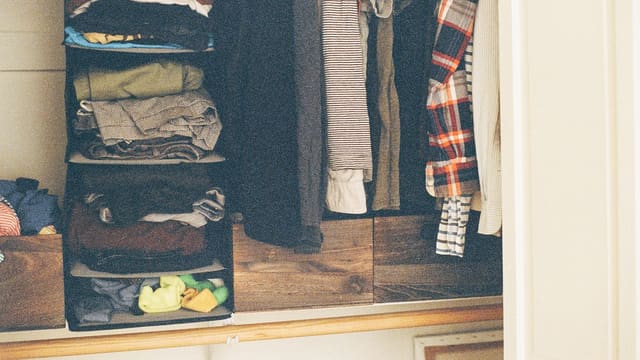 An open closet with folded sweaters and shirts on shelves and hangers.
