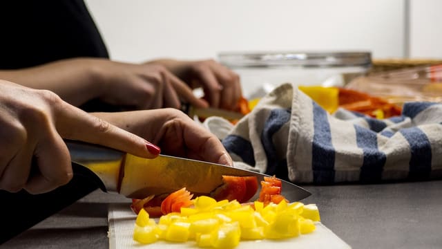 Hands chopping yellow peppers on a cutting board at home.