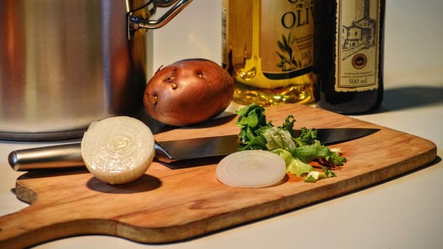Vegetables and a knife on a wooden cutting board in a home kitchen.