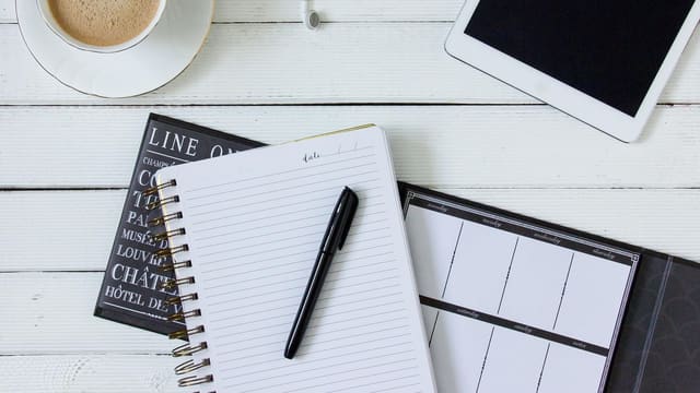 A cup of coffee made at home next to a notebook and pen.